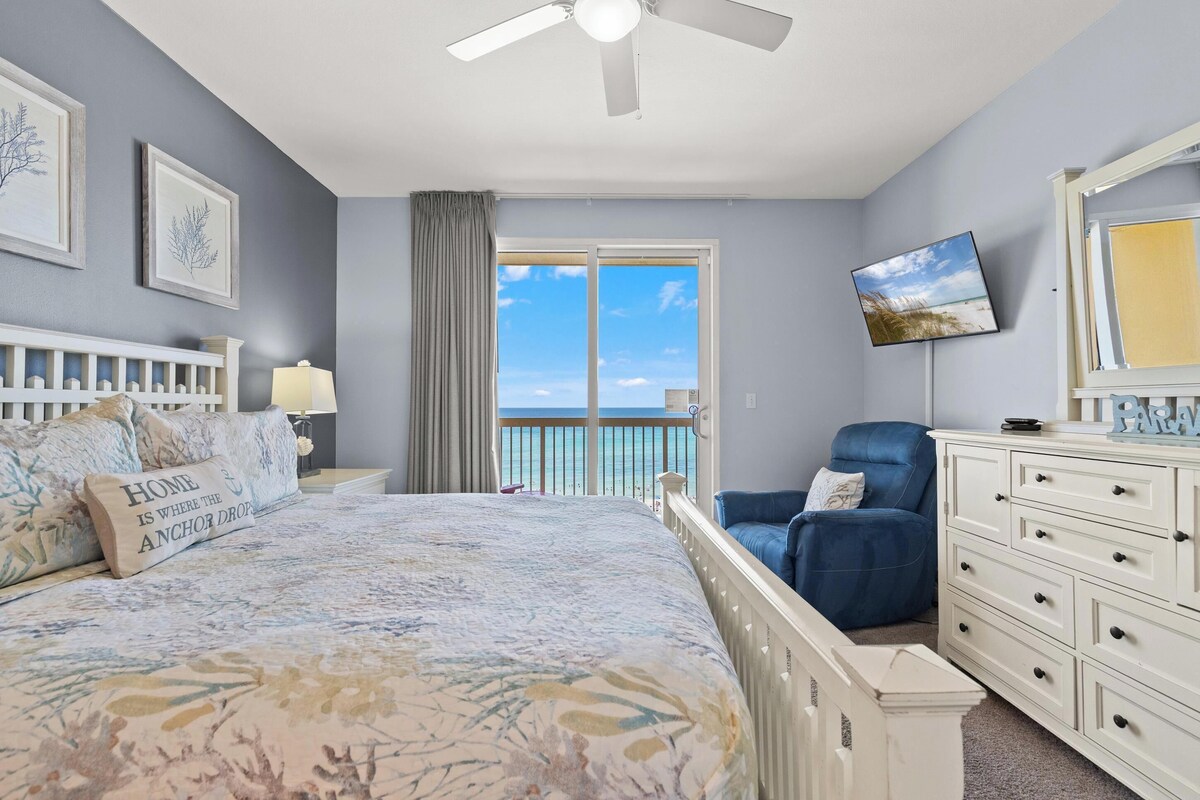 A bedroom with a bed, a dresser, a chair, a TV, and a balcony with a view.