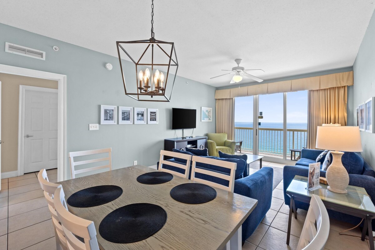 A modern living room with a dining area, a television, and a large window with a view of the ocean.