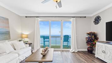 Un salon comprenant un canapé, une table basse, un ventilateur de plafond, un téléviseur, une plante et une vue sur l’océan grâce à de grandes portes coulissantes.