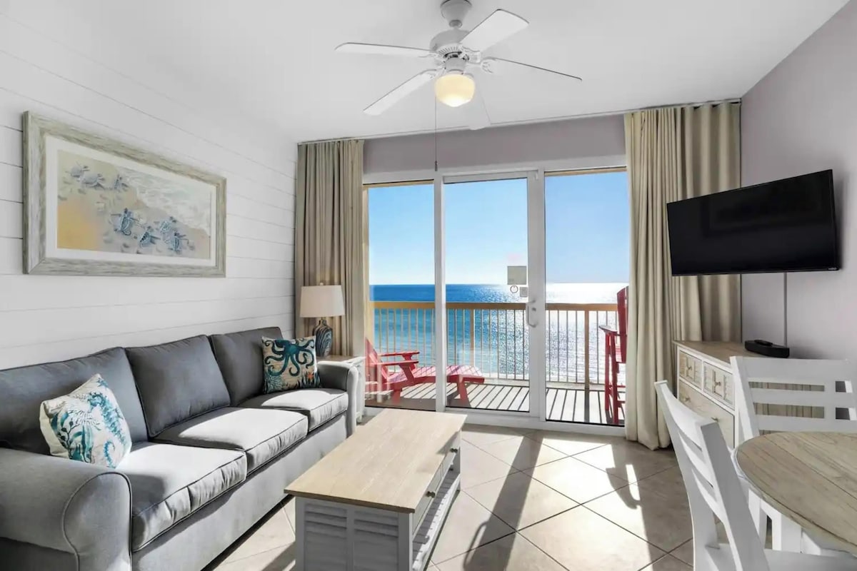 A hotel room with a balcony, a sofa, a coffee table, a TV, and a painting on the wall.