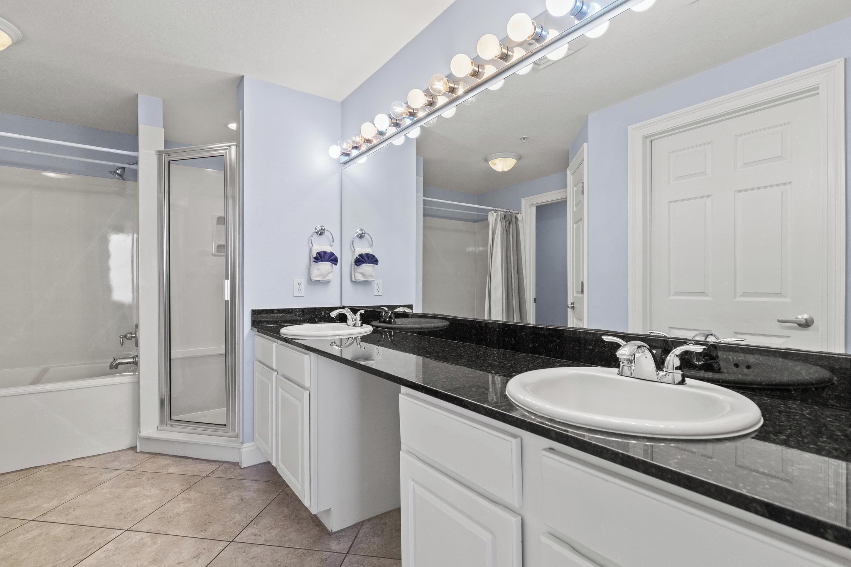 Une salle de bain avec deux lavabos, un grand miroir avec éclairage, une douche et une porte.