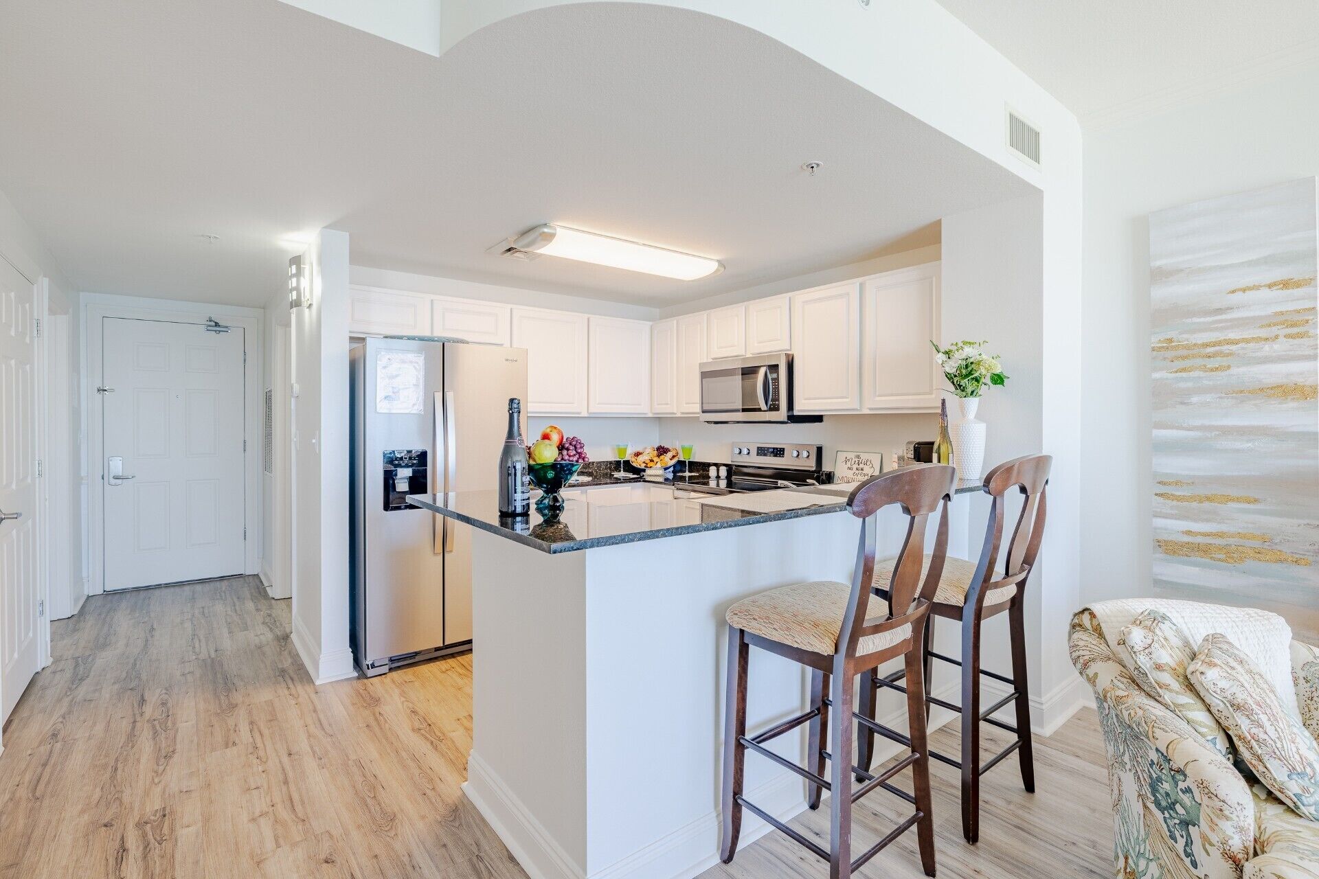 Una cocina moderna con armarios blancos, electrodomésticos de acero inoxidable y una isla central con taburetes de bar.