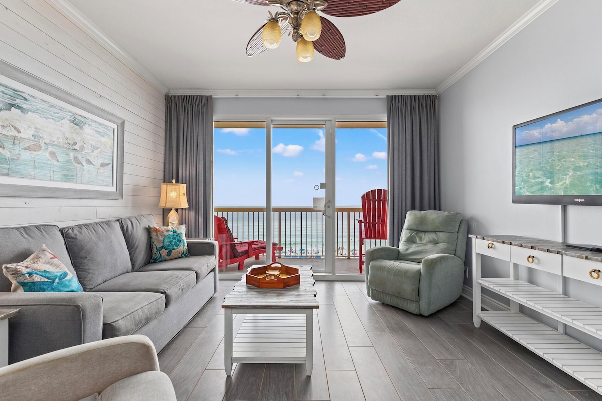 A modern living room with a grey sofa, a coffee table, a TV, and a balcony with red chairs.