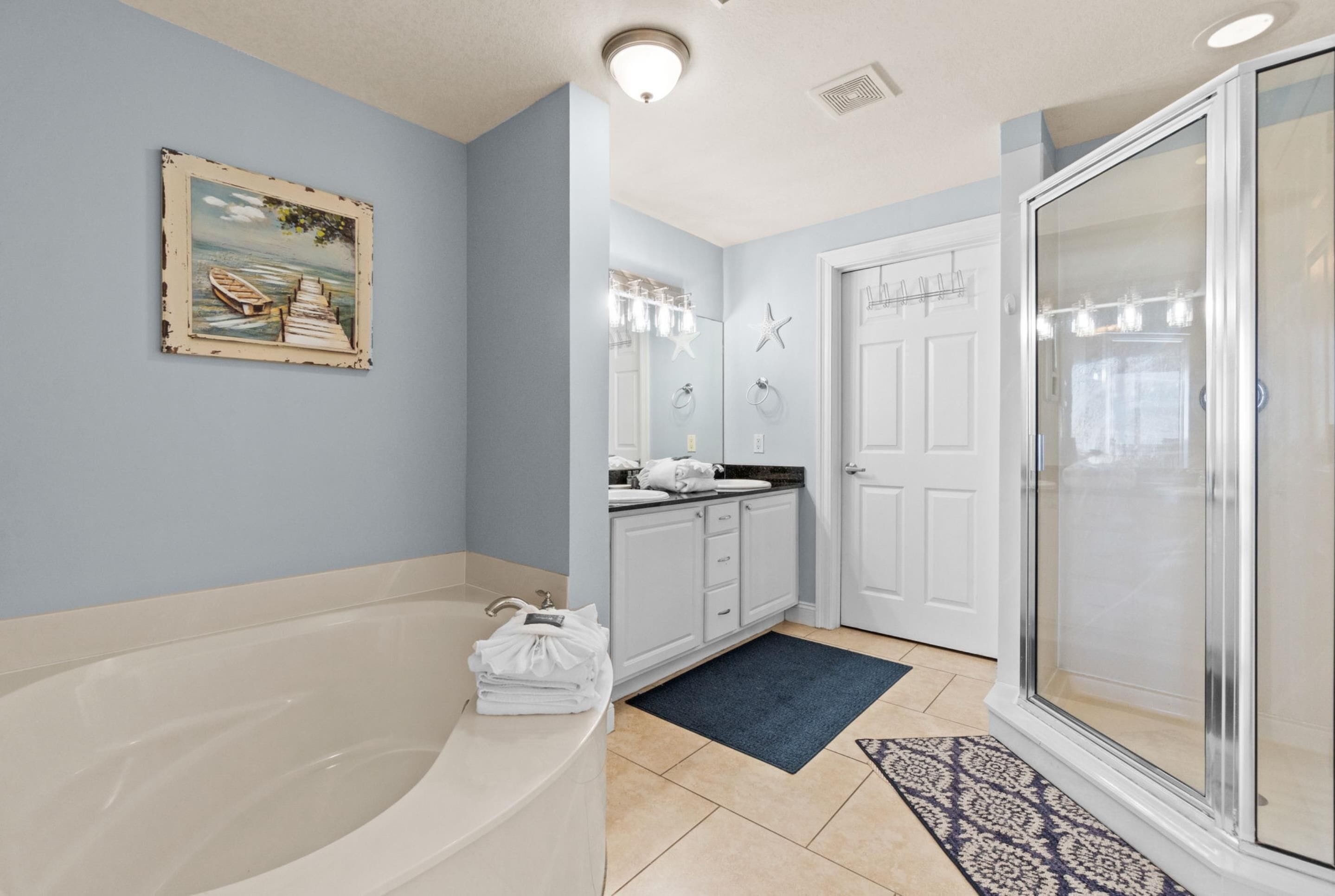 A bathroom with a bathtub, a shower, a sink with a mirror, and a door with a starfish decoration.