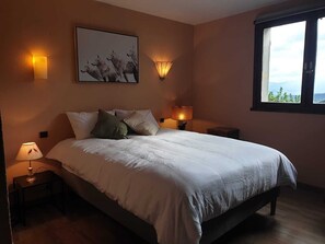 A bedroom with a bed, two bedside lamps, a wall-mounted picture, and a window with a view. - Cerdanya—House with a garden, 1 km from Llivia • 7 people • Near Font-Romeu. (Estavar)
