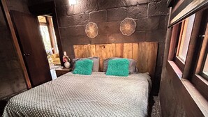 A bedroom with a stone wall, wooden headboard, patterned carpet, and a bed with a white blanket and green pillows. - Villas Bosque Alto By GEstores (Huasca de Ocampo)