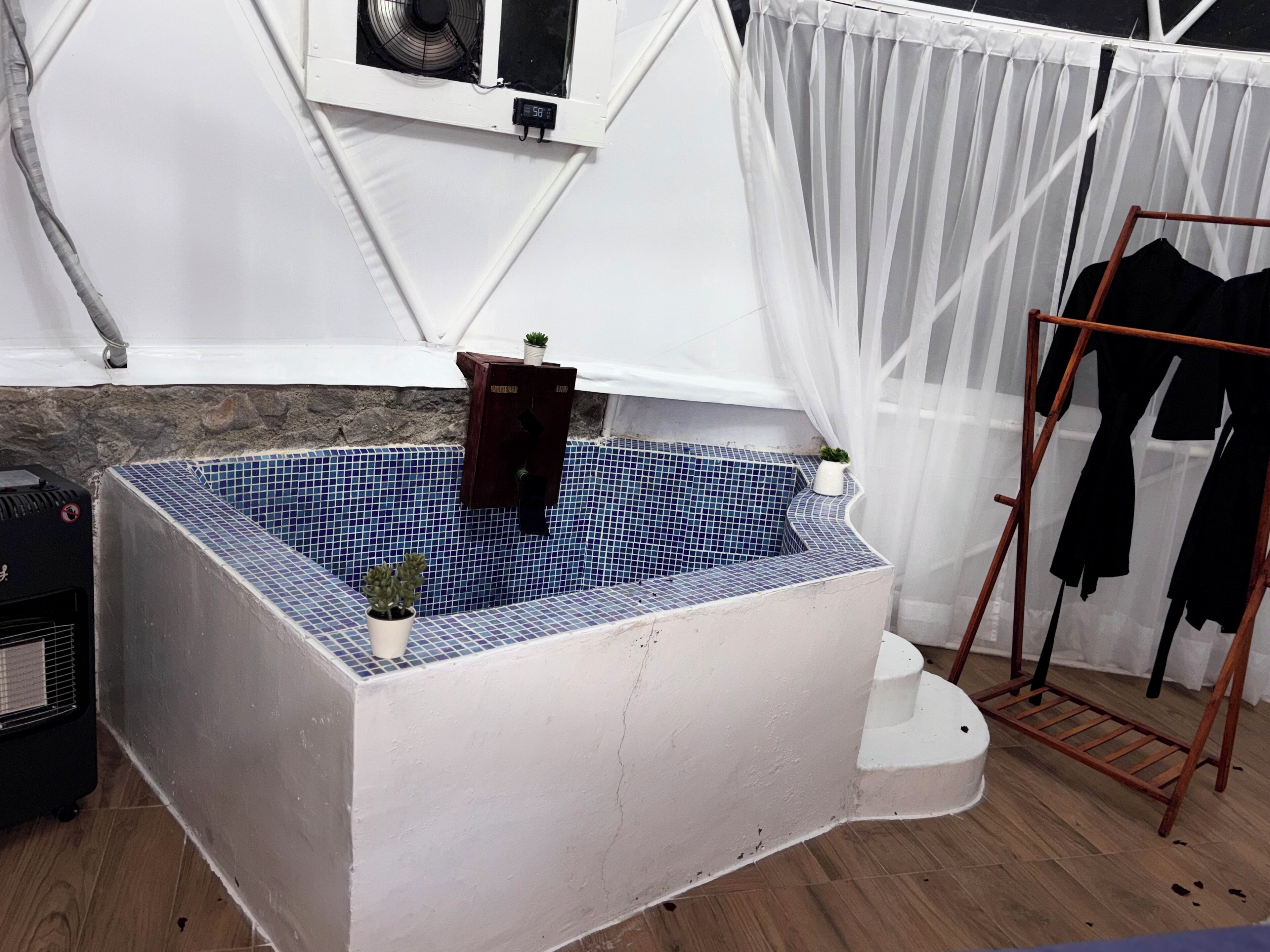 A room with a bathtub, a wooden rack, and a white curtain.
