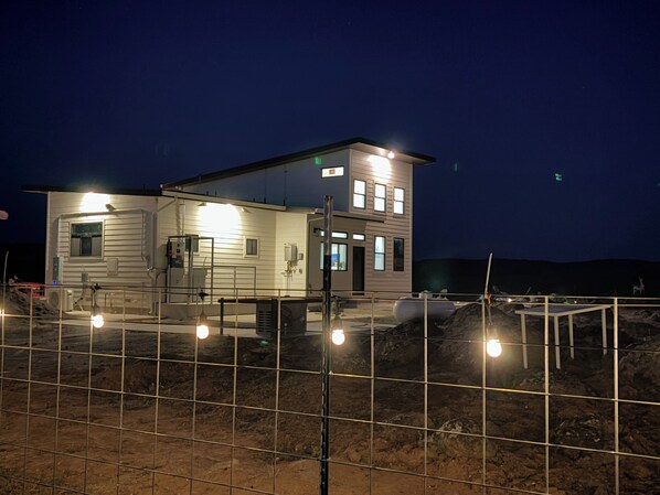 A two-story building with a flat roof, rectangular windows, and a fenced area in front.