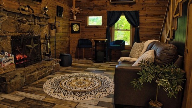 A cozy cabin interior with a stone fireplace, a round patterned rug, a leather sofa, and a potted plant. - Peaceful Nature Retreat In Eureka Springs (Eureka Springs)