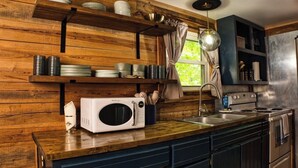 A kitchen with wooden shelves, a microwave, a stove, and a sink. - Peaceful Nature Retreat In Eureka Springs (Eureka Springs)