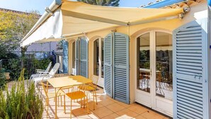 A covered outdoor patio with a table and chairs, a yellow awning, and blue shutters on the windows. - Villa Cannoise, Air-conditioned, Spacious, Sea view (Le Cannet)