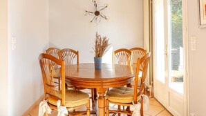 A dining area with a round wooden table, six chairs, a vase with dried plants, and a wall-mounted light fixture. - Villa Cannoise, Air-conditioned, Spacious, Sea view (Le Cannet)