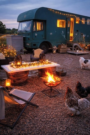 Eine rustikale Außenanlage mit einem Feuerkorb, einem Esstisch und einem Wohnwagen im Vintage-Stil im Hintergrund.. Out in the countryside,Retreat away@The Box