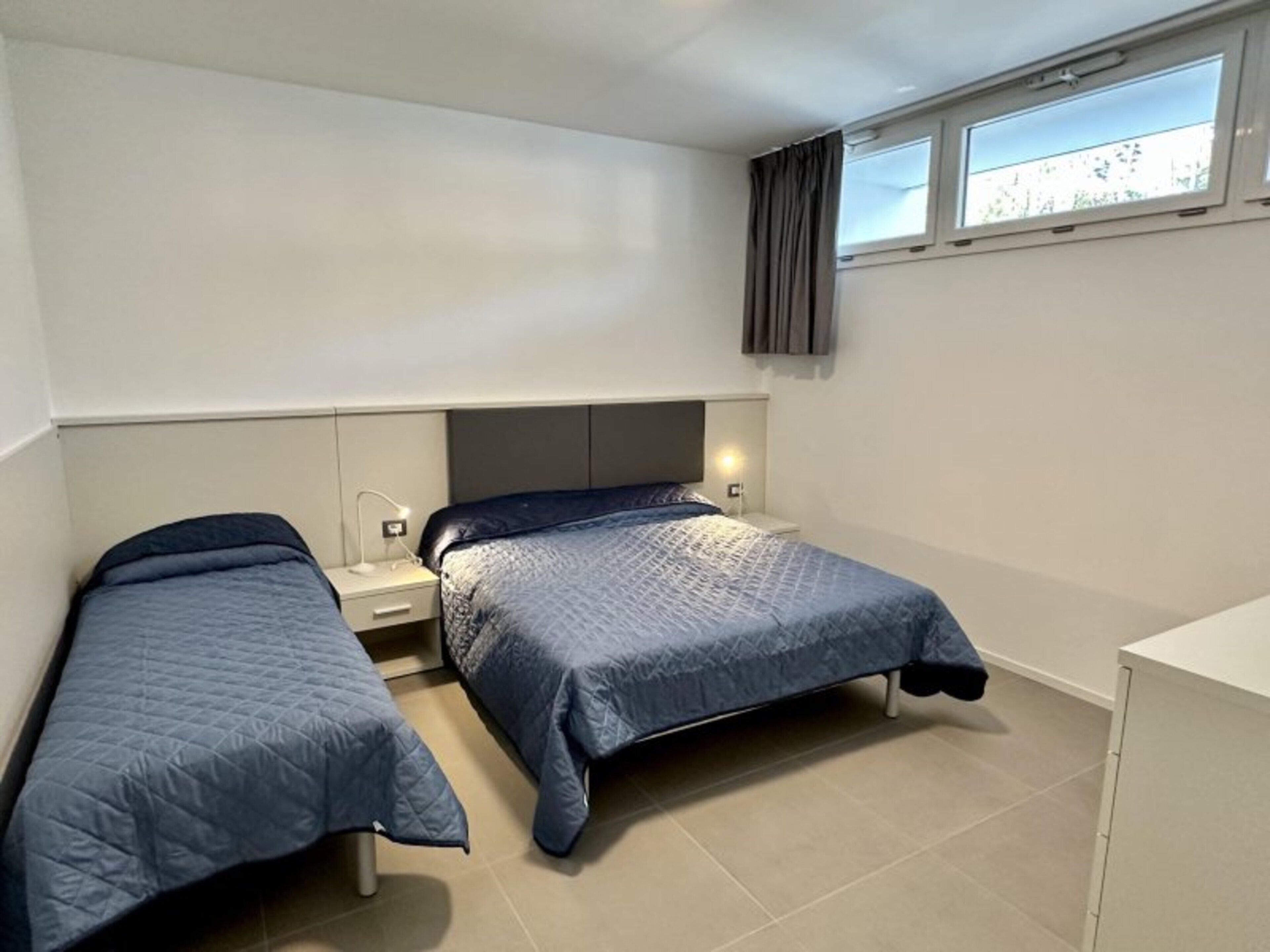 Ein Schlafzimmer mit zwei Betten, einem Fenster mit Vorhängen und einem Nachttisch mit Lampe.