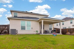 A two-story house with a covered patio, a fenced backyard, and a grill.