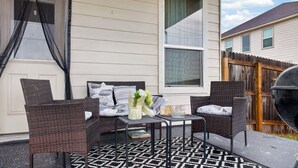 Un patio con mobiliario de mimbre, alfombra estampada y una ventana con cortina.