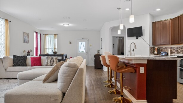 Una sala de estar moderna con un sofá, un comedor con sillas, una cocina con televisión y armarios de madera.