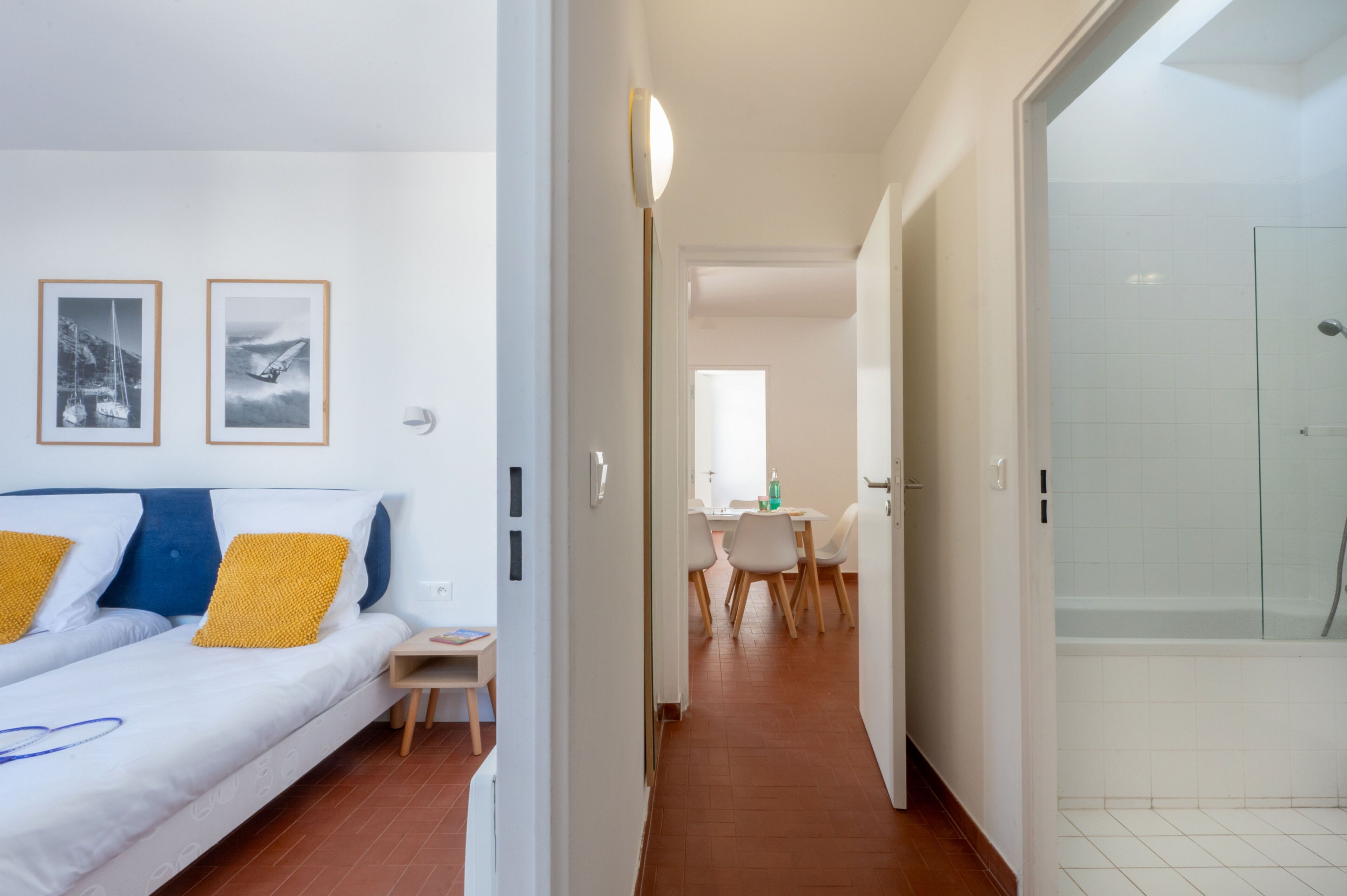A hotel room with a bed, a small table, a chair, a dining area, and a shower.