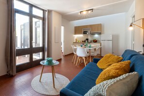 Un salon moderne avec un canapé bleu, une petite table ronde et une vue sur l’extérieur, visible à travers une porte vitrée.