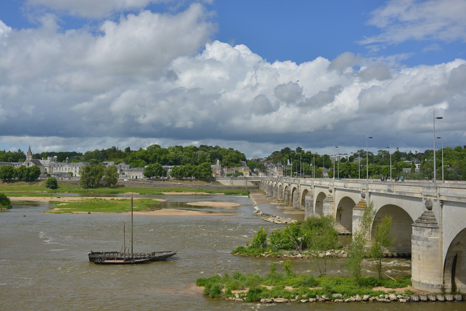 Une rivière avec un pont, un voilier et des bâtiments en arrière-plan.