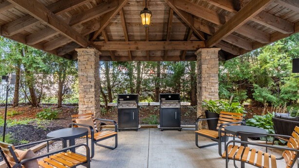An outdoor patio with stone pillars, wooden ceiling beams, and two barbecue grills.