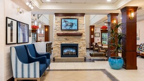 A lobby with a stone fireplace, blue sofas, a large potted plant, and framed artwork on the walls.