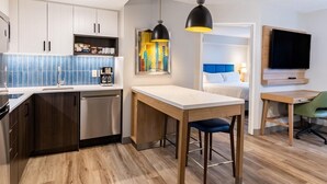 A compact kitchen with modern appliances, a dining area with a table and chairs, a flat-screen TV mounted on the wall, and a painting on the wall.