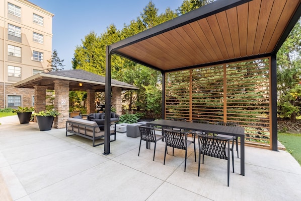 An outdoor patio with a covered seating area, a table, and chairs.
