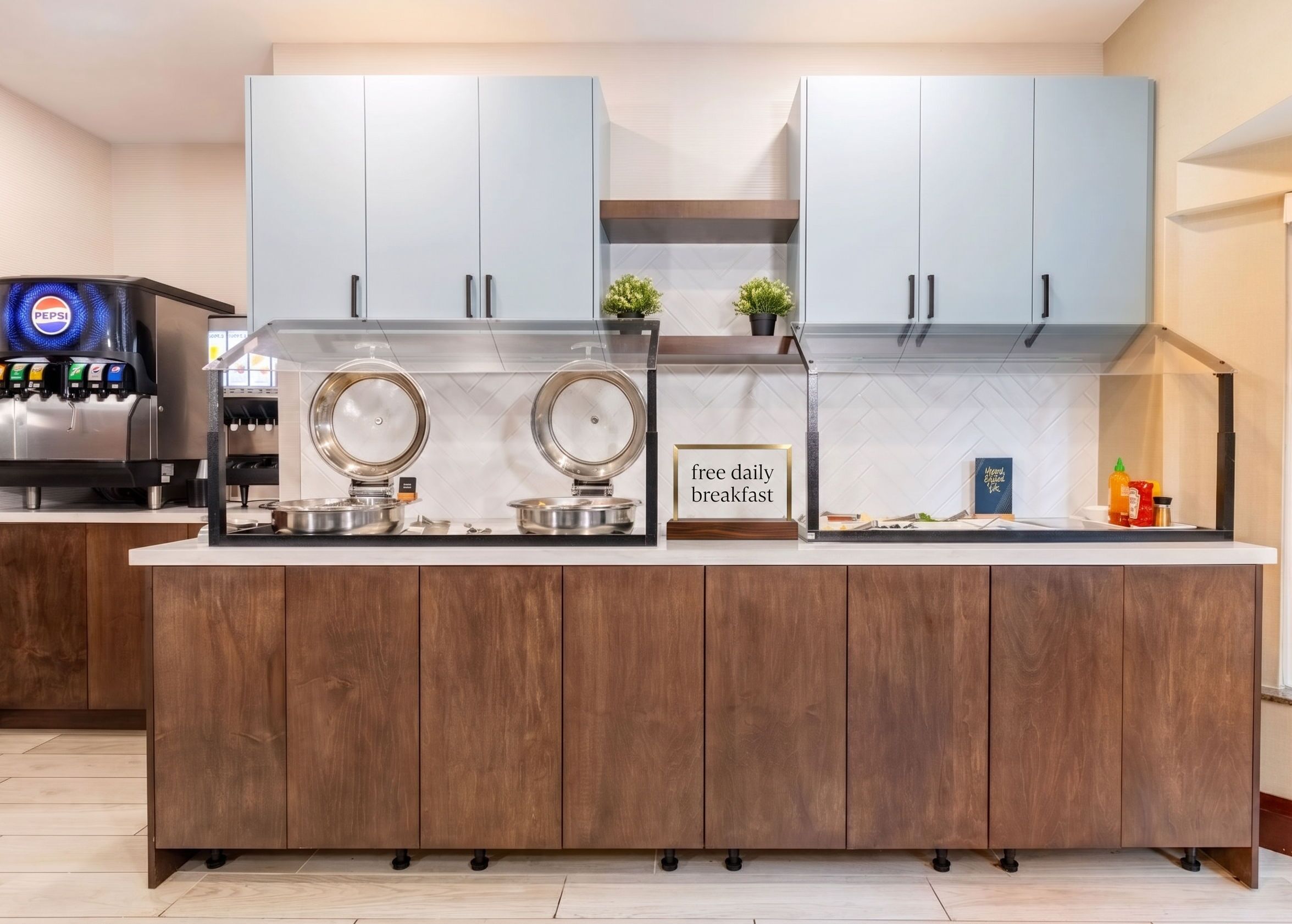 A modern kitchen with two large refrigerators, a coffee machine, and a sign offering free daily breakfast.