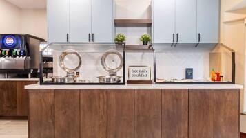 A modern kitchen with two large refrigerators, a coffee machine, and a sign offering free daily breakfast.