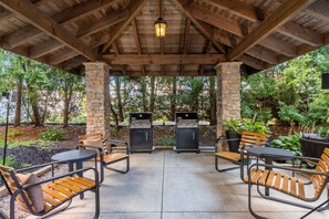 En uteplats med pelare av sten, träbjälkar i taket och två grillar.