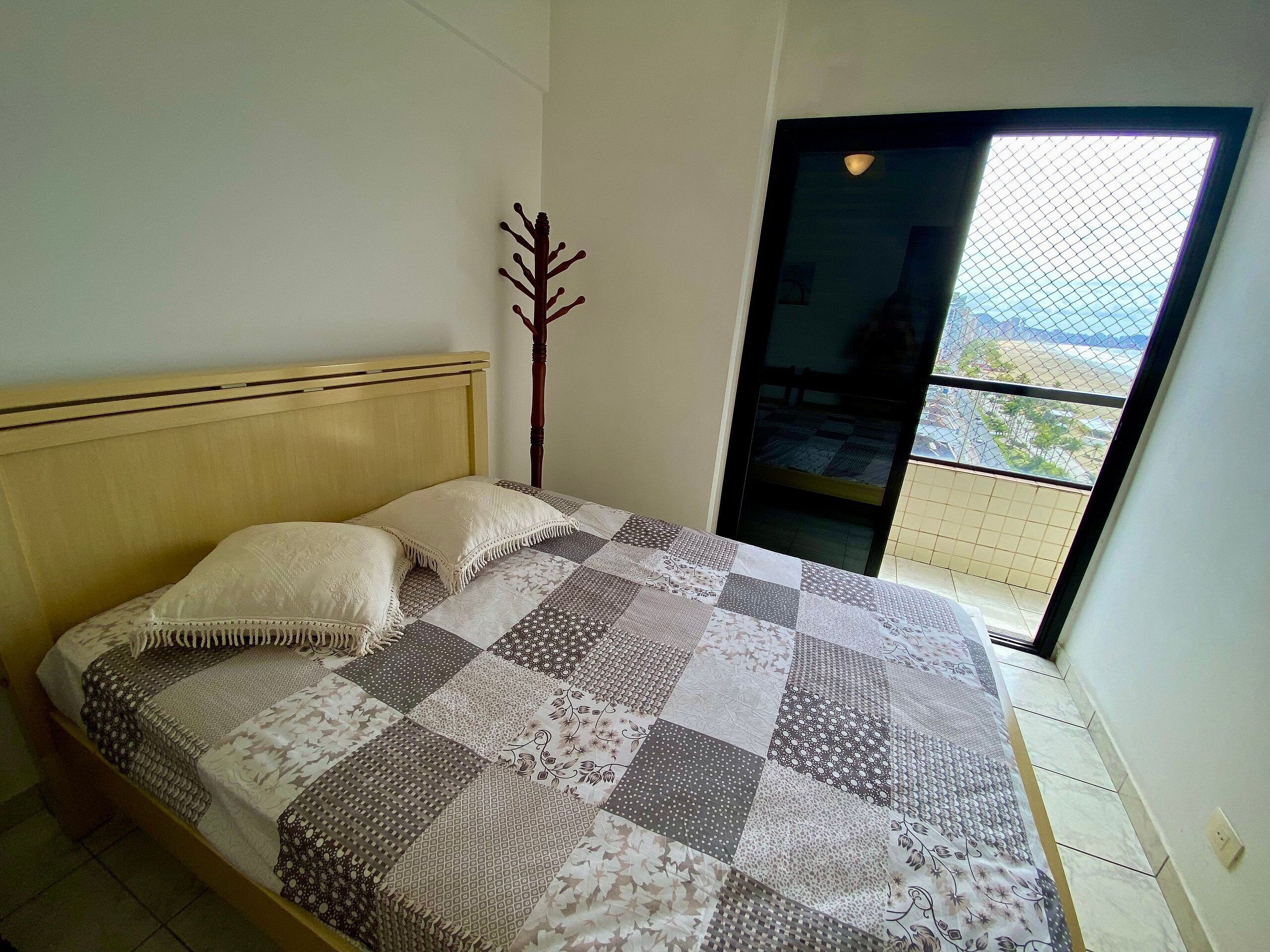 A bedroom with a bed, a wooden headboard, a decorative tree, and a view through a window.