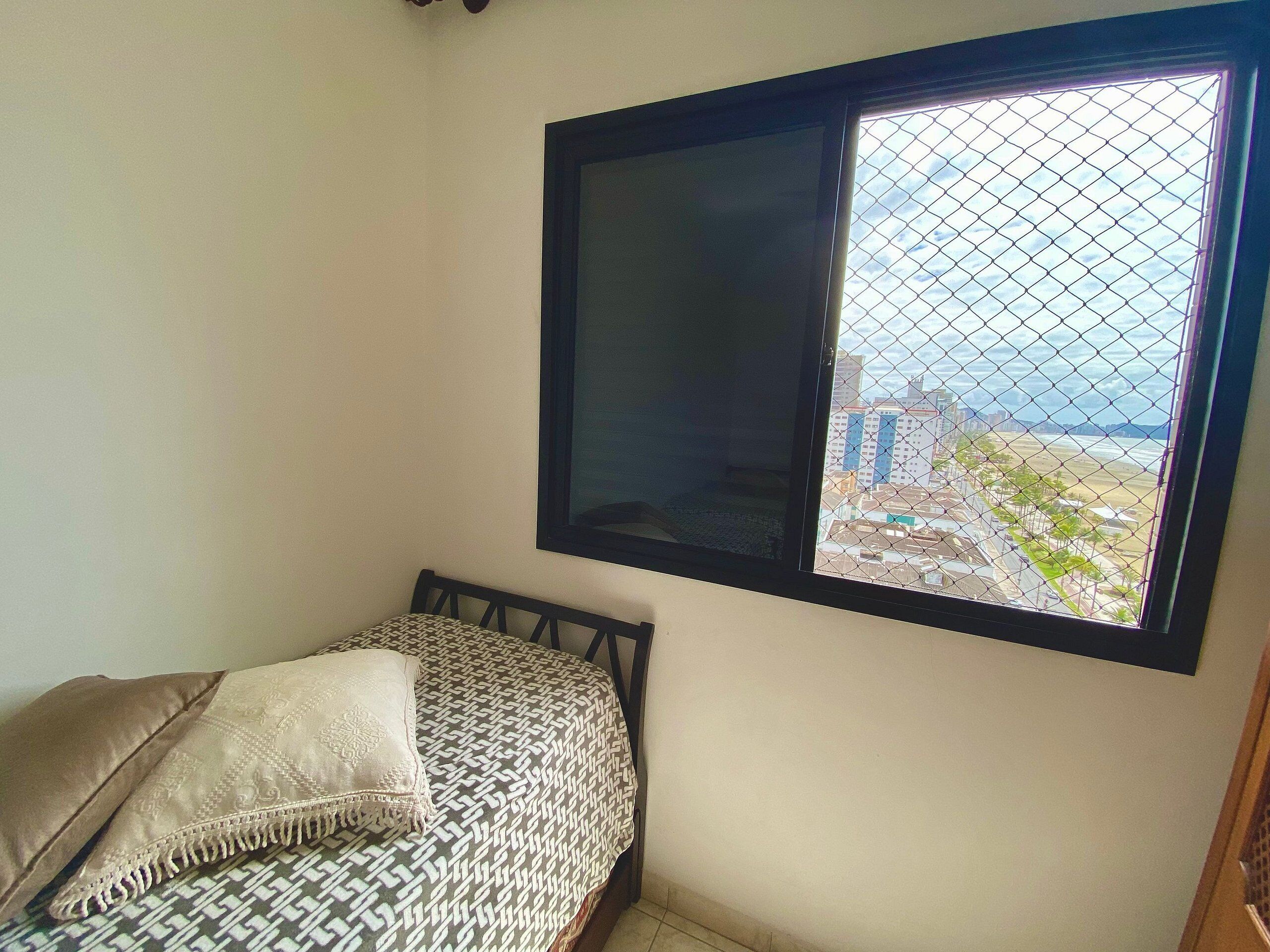 Une pièce avec un lit, une fenêtre donnant sur des immeubles et une porte.
