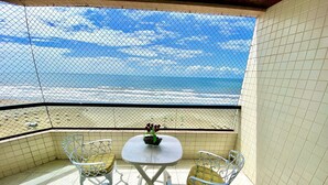 Ein Balkon mit Blick auf den Strand, zwei Stühle, ein kleiner Tisch und ein Blumentopf.