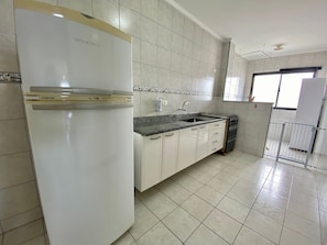 A kitchen with white cabinets, a granite countertop, a stainless steel refrigerator, and a gas stove. - Edifício Paulo Roberto (Praia Grande)