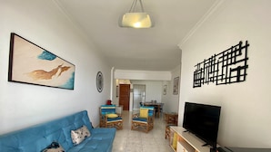 Ein Wohnzimmer mit einem blauen Sofa, einem Fernseher, einem Essbereich mit Stühlen und einer Küchenzeile mit einem roten Gerät.
