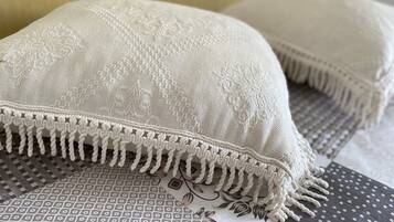 A close-up of a white textured pillow with a fringe detail, placed on a patterned fabric.
