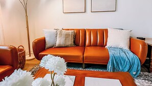 A living room with a brown leather sofa, two framed pictures on the wall, a floor lamp, and a vase with white flowers. - Modern House Near ACU, HSU, Hendrick North (Abilene)