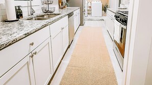 A narrow kitchen with white cabinets, a granite countertop, a built-in oven, and a stainless steel sink. - Modern House Near ACU, HSU, Hendrick North (Abilene)