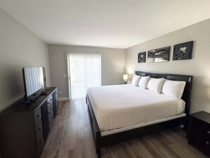 Ein Schlafzimmer mit Bett, Schminktisch, Fernseher und einem Fenster mit Jalousien.