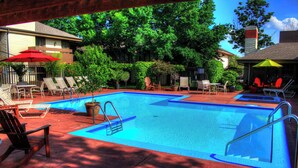 A swimming pool with lounge chairs and umbrellas, surrounded by trees and a building. - One Bedroom,  First Floor (Wichita)