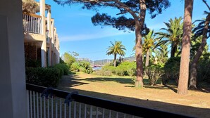 Un balcón con mesa y sillas, con vista a un jardín de palmeras y una construcción distante.