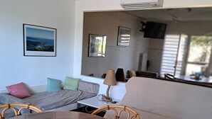 Una habitación con una mesa de comedor redonda, sillas de mimbre, un sofá y un espejo grande.