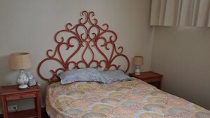 Una cama con colcha estampada, un cabecero decorativo, dos mesitas de noche con lámparas y un suelo de baldosas.