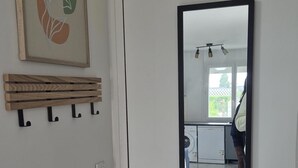 A white door with a large mirror reflecting a kitchen area, a wooden coat rack, and a wall-mounted light fixture. - Le Cocon : Bright studio 32m² + free private parking (rare). Near Stadium (Troyes)