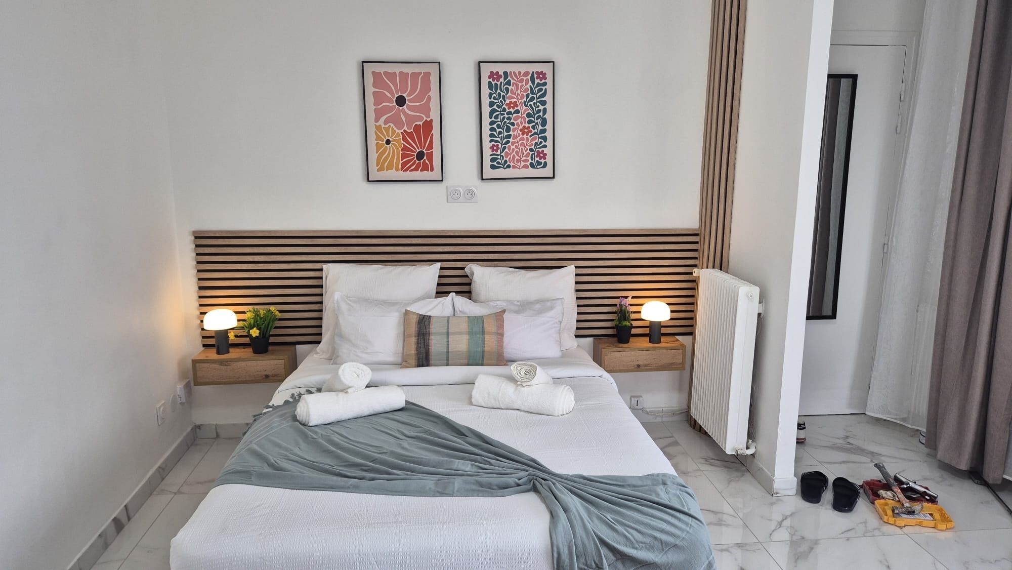 Un letto rifatto con cuscini e coperta, comodini con lampade, e due opere d'arte appese al muro.