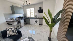 A modern kitchen with a dishwasher, washing machine, and a dining area with a sofa and coffee table. - Le Cocon : Bright studio 32m² + free private parking (rare). Near Stadium (Troyes)