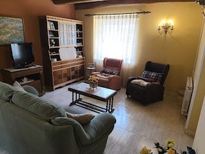 Una sala de estar con un sofá, una silla, una mesa de centro, un televisor, un mueble y una ventana con cortinas.