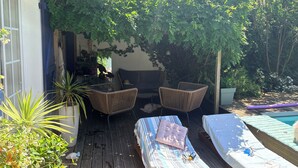 Een overdekt terras met rieten meubilair, een comfortabele bank en een zwembad.