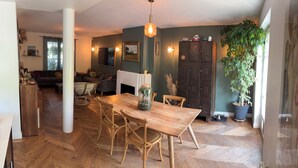 Een eethoek met een houten tafel en stoelen, een hanglamp en een grote potplant.